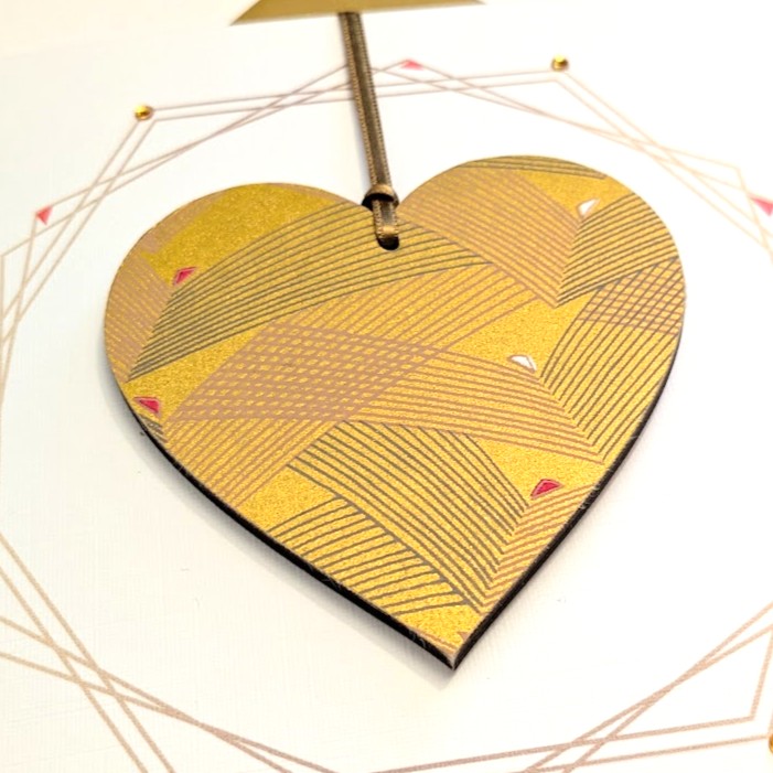 Square handmade greeting card with a gold envelope. The card features a printed geometric wreath with applied crystals. In the centre, a wooden heart ornament is suspended by a gold ribbon. The front of the wooden heart is hand-decoupaged with authentic Japanese Chiyogami paper featuring metallic gold abstract bird patterns.