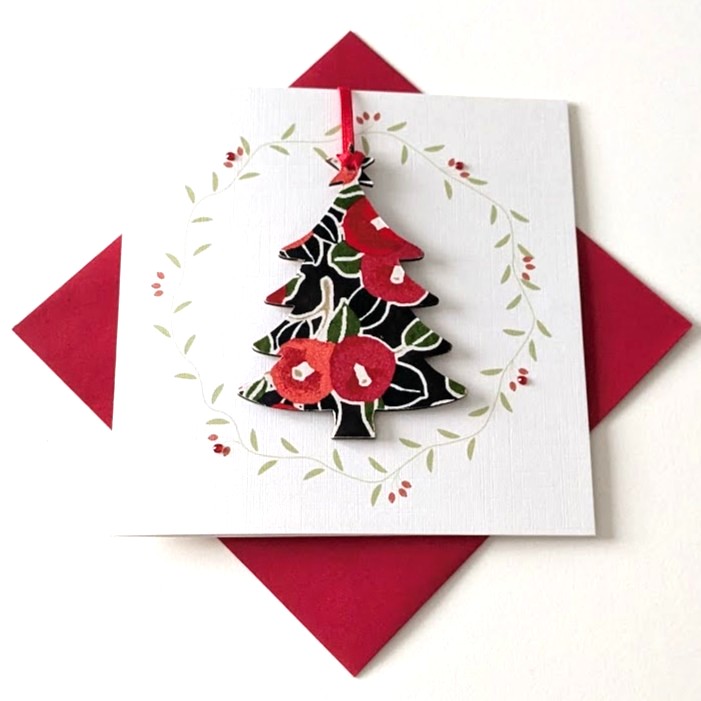 Square handmade greeting card with a red envelope. The card features a printed vine wreath with applied crystals. In the centre, a wooden tree shaped ornament is suspended by a red ribbon. The front of the wooden tree is hand-decoupaged with authentic Japanese Chiyogami paper featuring a red berries and leaf pattern with metallic gold accents.