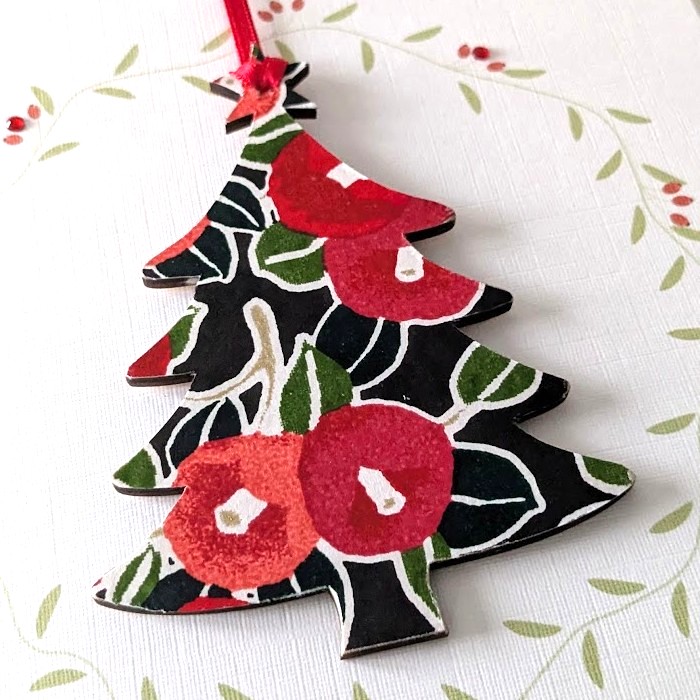 Square handmade greeting card with a red envelope. The card features a printed vine wreath with applied crystals. In the centre, a wooden tree shaped ornament is suspended by a red ribbon. The front of the wooden tree is hand-decoupaged with authentic Japanese Chiyogami paper featuring a red berries and leaf pattern with metallic gold accents.