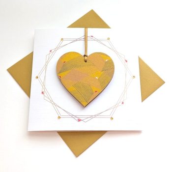Square handmade greeting card with a gold envelope. The card features a printed geometric wreath with applied crystals. In the centre, a wooden heart ornament is suspended by a gold ribbon. The front of the wooden heart is hand-decoupaged with authentic Japanese Chiyogami paper featuring metallic gold abstract bird patterns.