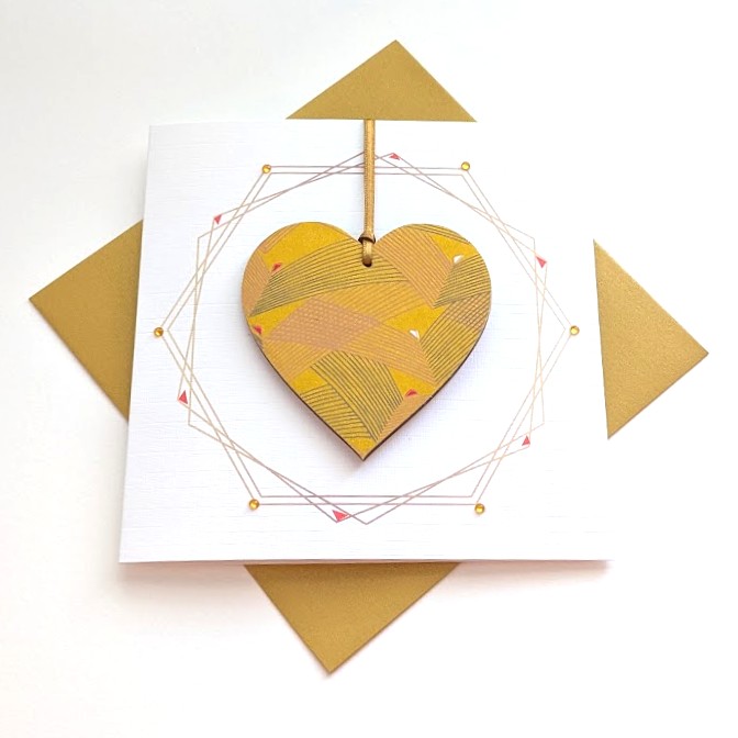 Square handmade greeting card with a gold envelope. The card features a printed geometric wreath with applied crystals. In the centre, a wooden heart ornament is suspended by a gold ribbon. The front of the wooden heart is hand-decoupaged with authentic Japanese Chiyogami paper featuring metallic gold abstract bird patterns.